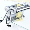 A chrome pasta maker is shown on a glass surface with newly made pasta strands hanging from it. Náhľad obrázku produktu