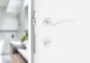 A close-up view of a white door handle and lock mechanism. Produktbild-Vorschau