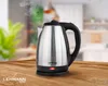 A stainless steel electric kettle is on a wooden table with steam rising from its spout, set against a blurred kitchen background. The brand logo and a red indicator light are visible. Podgląd zdjęcia produktu