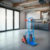 A blue and red hand truck with stair-climbing wheels is shown in a garage or workshop setting. Náhled obrázku produktu