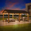 An outdoor patio area at dusk, featuring a wooden pergola with string lights, outdoor furniture, and a modern house in the background. Náhled obrázku produktu
