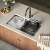 A modern kitchen sink area with dishes being washed and a drying rack. Produktbild-Vorschau