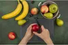 A top-down view of hands preparing fruit on a cutting board, surrounded by various fruits and a bowl. Anteprima dell’immagine prodotto