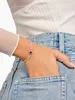 A woman's hand wearing a bracelet is placed in the pocket of her denim jeans. Podgląd zdjęcia produktu
