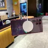 A purple phone case with a magnetic charging ring is shown hanging in what appears to be a cafe or retail environment. Náhled obrázku produktu