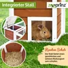 A rabbit in a wooden hutch with straw bedding, set in a grassy outdoor environment. The image includes text overlays and a logo. Produktbild-Vorschau