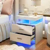 A modern white nightstand with LED lighting next to a bed. Náhled obrázku produktu