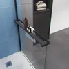 A modern shower enclosure with a black frame, glass panels, and a shelf holding toiletries and towels. Produktbild-Vorschau