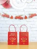 Two red gift bags with fire truck themed decorations are displayed on a wooden surface in front of a white brick wall decorated with fire truck and flame garland and paper fans. Podgląd zdjęcia produktu