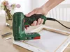A hand holding a green electric tacker, using it to attach canvas to a wooden frame. Produktbild-Vorschau