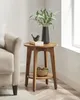 A wooden round side table next to a sofa, with a vase of greenery, a book, and a decorative bird on top. Produktbild-Vorschau