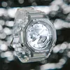 A close-up shot of a transparent G-Shock watch with a silver face, set against a blurred background of bokeh lights. Produktbild-Vorschau