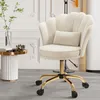 A beige velvet office chair with a shell-shaped back and gold legs is shown in a room with white paneled walls and a small side table. Voir les images du produit