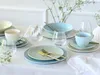 A table setting with pastel-colored porcelain dishes, glasses, and cutlery, arranged on a white tablecloth. Náhľad obrázku produktu