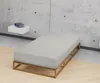 A minimalist bedroom scene with a bed frame and mattress against a concrete wall. Produktbild-Vorschau