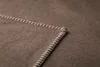 A close-up view of a corner of a brown blanket with white stitching along the edge. Produktbild-Vorschau