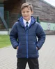 A young boy wearing a school uniform and a padded jacket stands outside a building. Produktbild-Vorschau