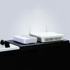 A shelf is attached to the top of a black screen, holding a white router and a white device with fans. Produktbild-Vorschau