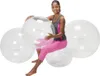 A woman is sitting on a large, clear exercise ball surrounded by other similar balls. Produktbild-Vorschau