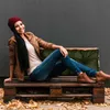 A woman is sitting on a pallet sofa with a green cushion, surrounded by fallen leaves. Náhled obrázku produktu