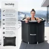 A woman is sitting in a portable ice bath tub outdoors with a snowy mountain landscape in the background. Náhled obrázku produktu