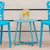 A blue metal side table with a pitcher of lemonade and a glass on it, flanked by two blue chairs, set against a white wall with black stripes. Voir les images du produit