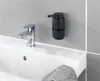 A black soap dispenser mounted on a tiled wall above a white sink with a chrome faucet. Produktbild-Vorschau