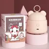 A pink cartoon-style mini desk vacuum cleaner is displayed next to its packaging, which features a drawing of a cat character. The background is a soft pink and gray. Náhled obrázku produktu