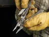 Hands wearing work gloves holding a Leatherman multitool. Produktbild-Vorschau