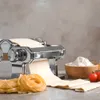 A pasta machine with dough, fresh pasta, flour, and tomatoes on a countertop. Podgląd zdjęcia produktu