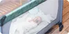 A baby is lying in a travel crib with a stuffed animal. Náhled obrázku produktu