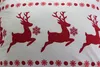 A close-up view of a white fabric with a repeating pattern of red reindeer and snowflakes. Podgląd zdjęcia produktu