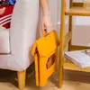 A person is holding a folded yellow stool next to a couch and a shelf. Produktbild-Vorschau