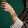 A person's wrist wearing a gold digital watch against a green background. Náhľad obrázku produktu