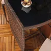 A close-up view of a wicker table with a glass top, placed on a wooden deck. Anteprima dell’immagine prodotto