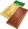 A gold-wrapped Merci chocolate bar and an unwrapped Merci chocolate bar with nuts are displayed diagonally on a white background. Produktbild-Vorschau