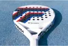 A close-up shot of a white padel racket with red, white, and blue accents, resting on a blue surface. Produktbild-Vorschau
