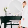 A woman in a bathrobe stands next to a vanity with a mirror and toiletries. Anteprima dell’immagine prodotto