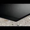 A close-up view of the edge of a black induction hob resting on a speckled countertop. Voir les images du produit