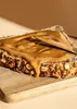 A slice of multi-grain bread spread with almond butter on a wooden cutting board. Produktbild-Vorschau