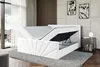 A modern bedroom with a white upholstered bed frame, featuring a lifted mattress to reveal storage space underneath. The room has a large window with sheer curtains, a textured wall panel, and two framed artworks on the wall. Produktbild-Vorschau