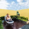 A woman and a child are reading a book on a chair on a wooden deck, with plants and a yellow fence in the background. Produktbild-Vorschau
