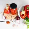 A collection of red bell peppers, onions, garlic, spices, and a jar of preserved peppers arranged on a white surface with a wooden cutting board. Podgląd zdjęcia produktu