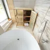 A bathroom with a bathtub, a wooden shelving unit, and a shower head. Produktbild-Vorschau