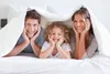 A family is lying in bed under a duvet, smiling at the camera. Produktbild-Vorschau