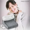 A woman is smiling and holding her neck while a foot warmer is in the foreground. Produktbild-Vorschau