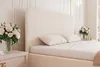A close-up view of a bed with a cream-colored headboard and pillows, next to a nightstand with a bouquet of roses. Náhled obrázku produktu