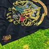 A close-up shot of a black blanket with the Hogwarts crest embroidered on it, laid out on green grass. Anteprima dell’immagine prodotto