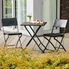 A small folding table and two chairs set up on a wooden deck, with plants in the foreground. Anteprima dell’immagine prodotto