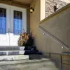 A stainless steel handrail is installed on the exterior wall next to a set of concrete stairs leading up to a double door entrance of a house. Náhled obrázku produktu